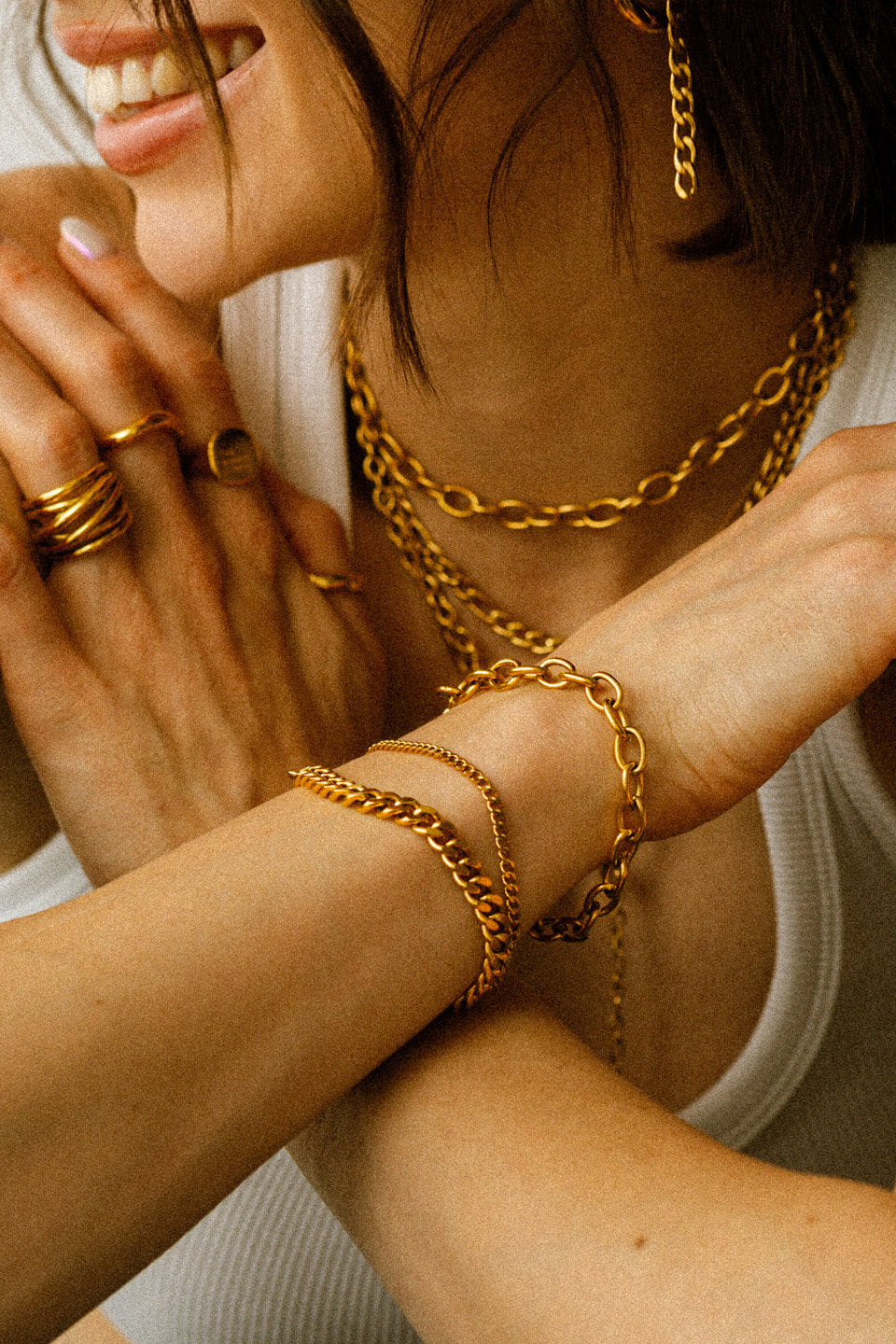 Verschränkte Arme mit auffälligen Armbändern, Ringen und Halsketten in Gold