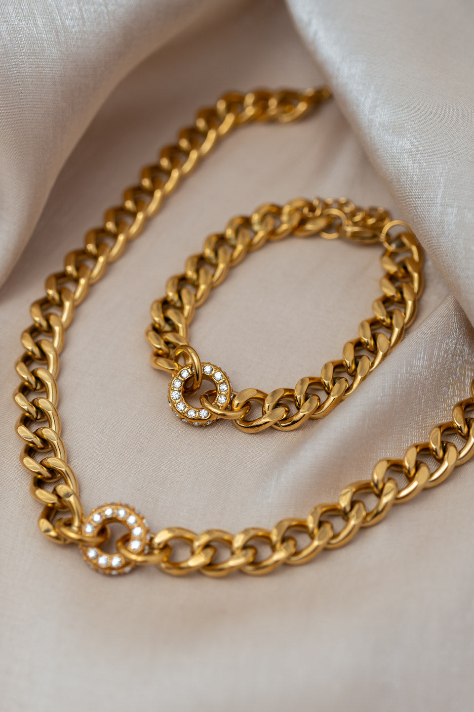 Schmuckset aus Kette und Armband in Gold, beide Schmuckstücke sind aus breiten Gliedern und haben in der Mitte einen runden, mit Zirkonia Steinen besetzen Anhänger