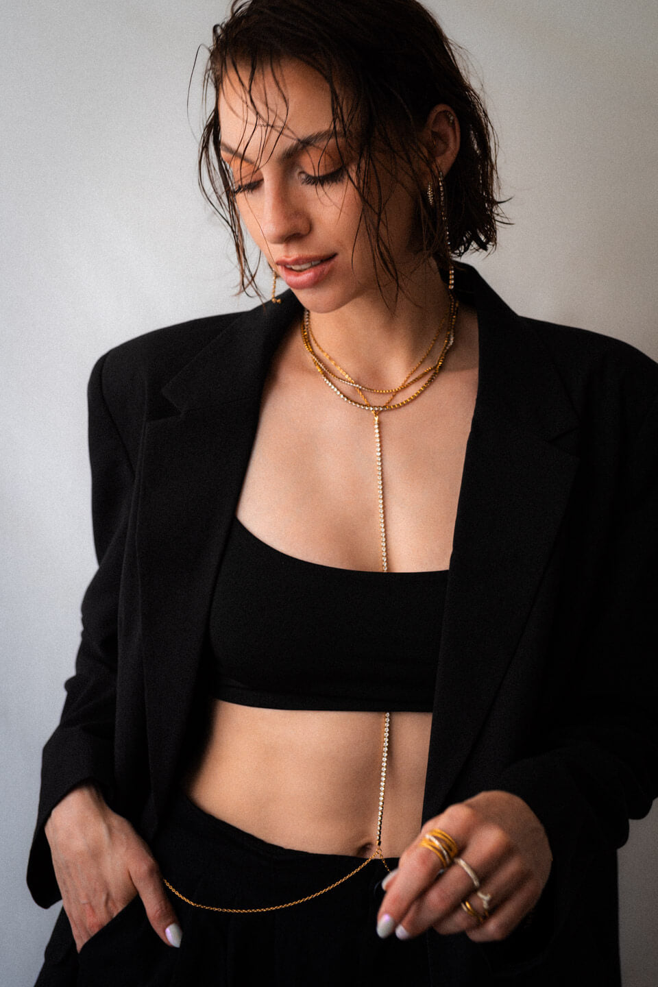 Junge Frau mit schwarzem Blazer und Crop Top, die viel Goldschmuck und eine Body Chain trägt